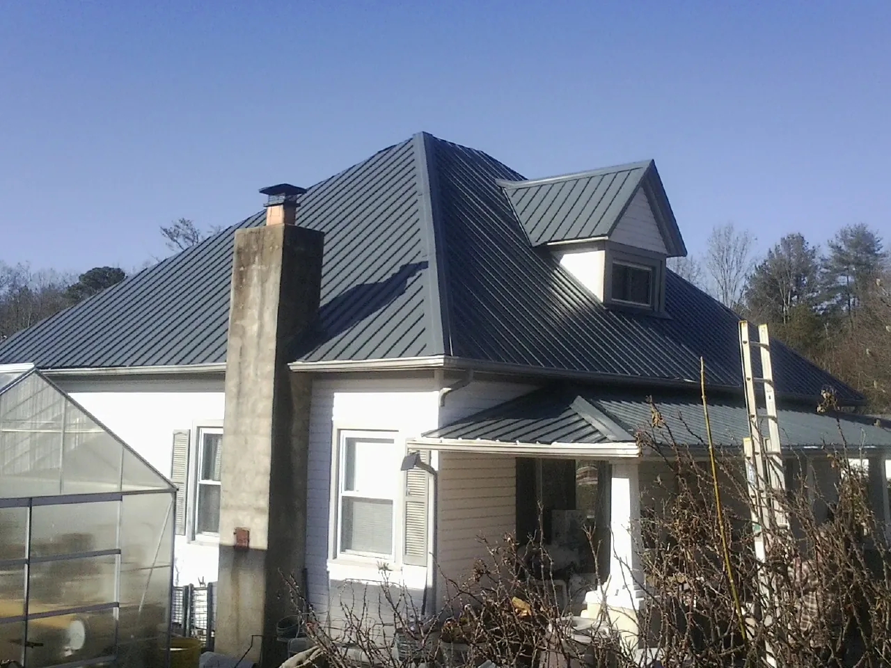 Dark blue standing seam metal roof on a white farmhouse with dormer — Slate & Tile Roof Repair by Roofing Brothers in Janesville