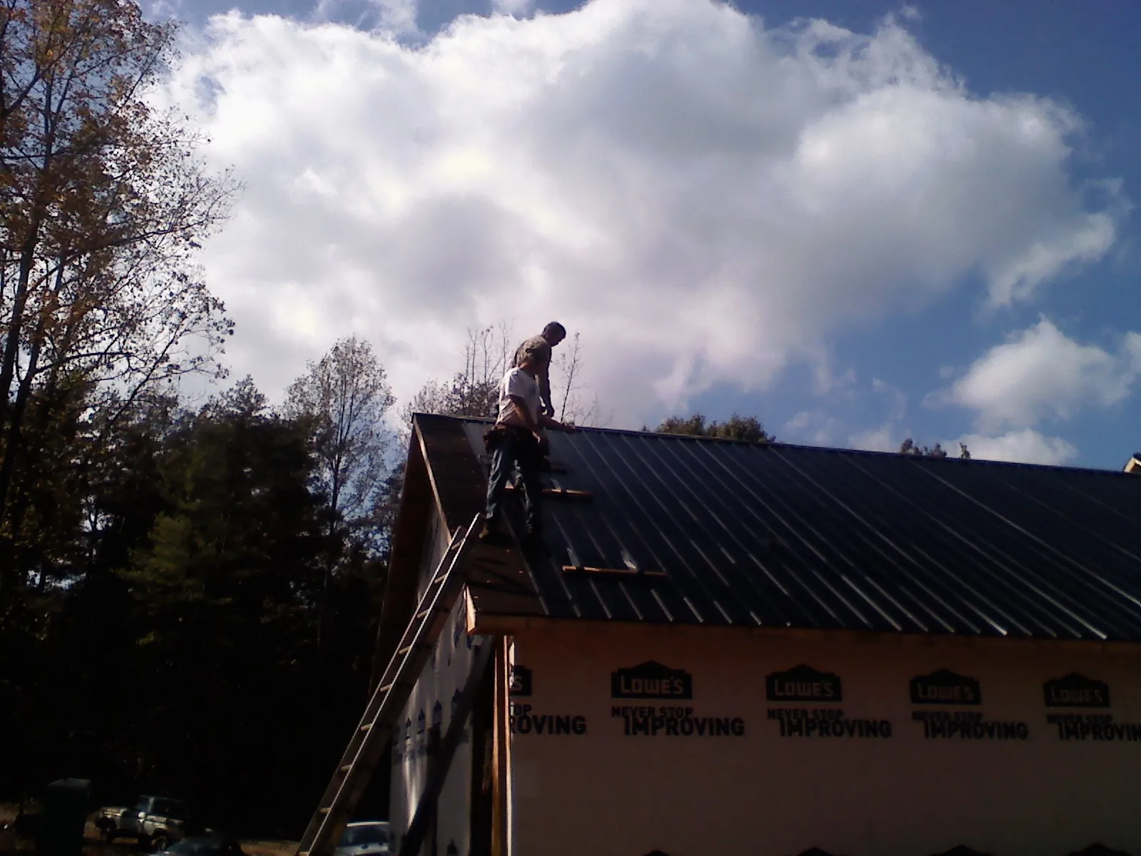 Roofer fastening dark metal panels high against a cloudy sky, from a Roof Inspection job in Janesville