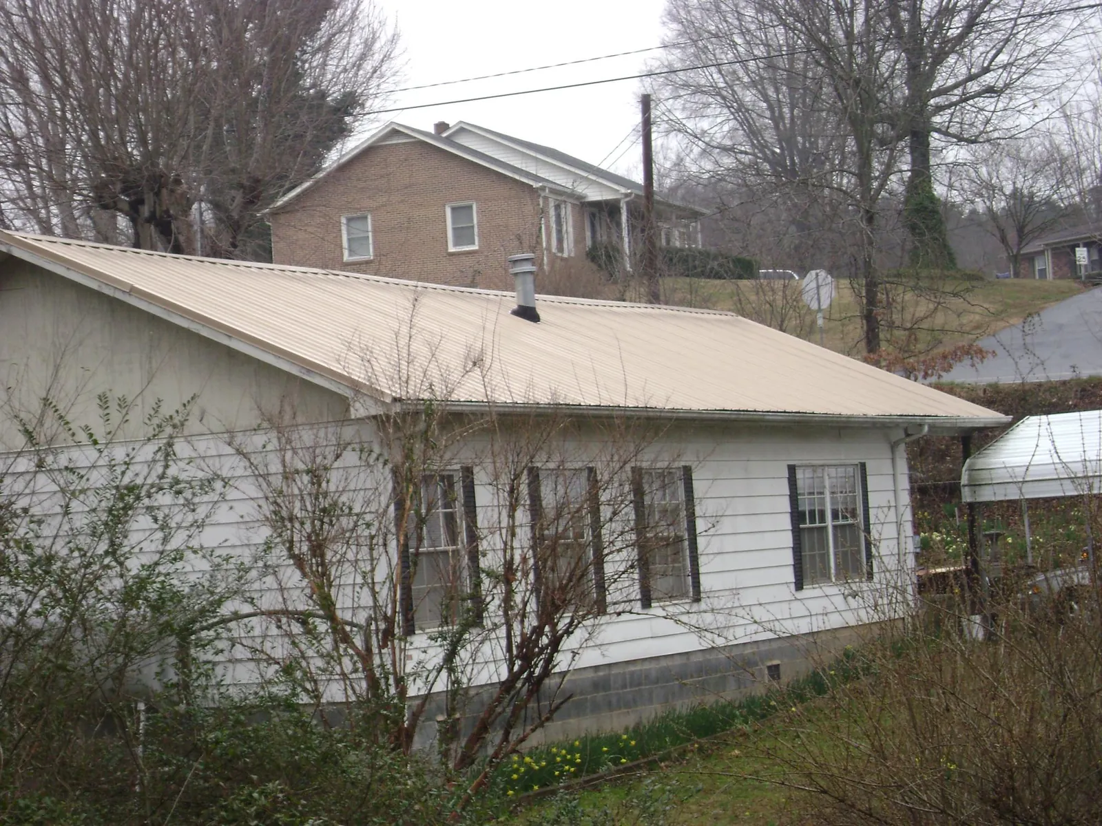 Tan metal roof on a white sided house set into a hillside — Commercial Roofing by Roofing Brothers in Janesville